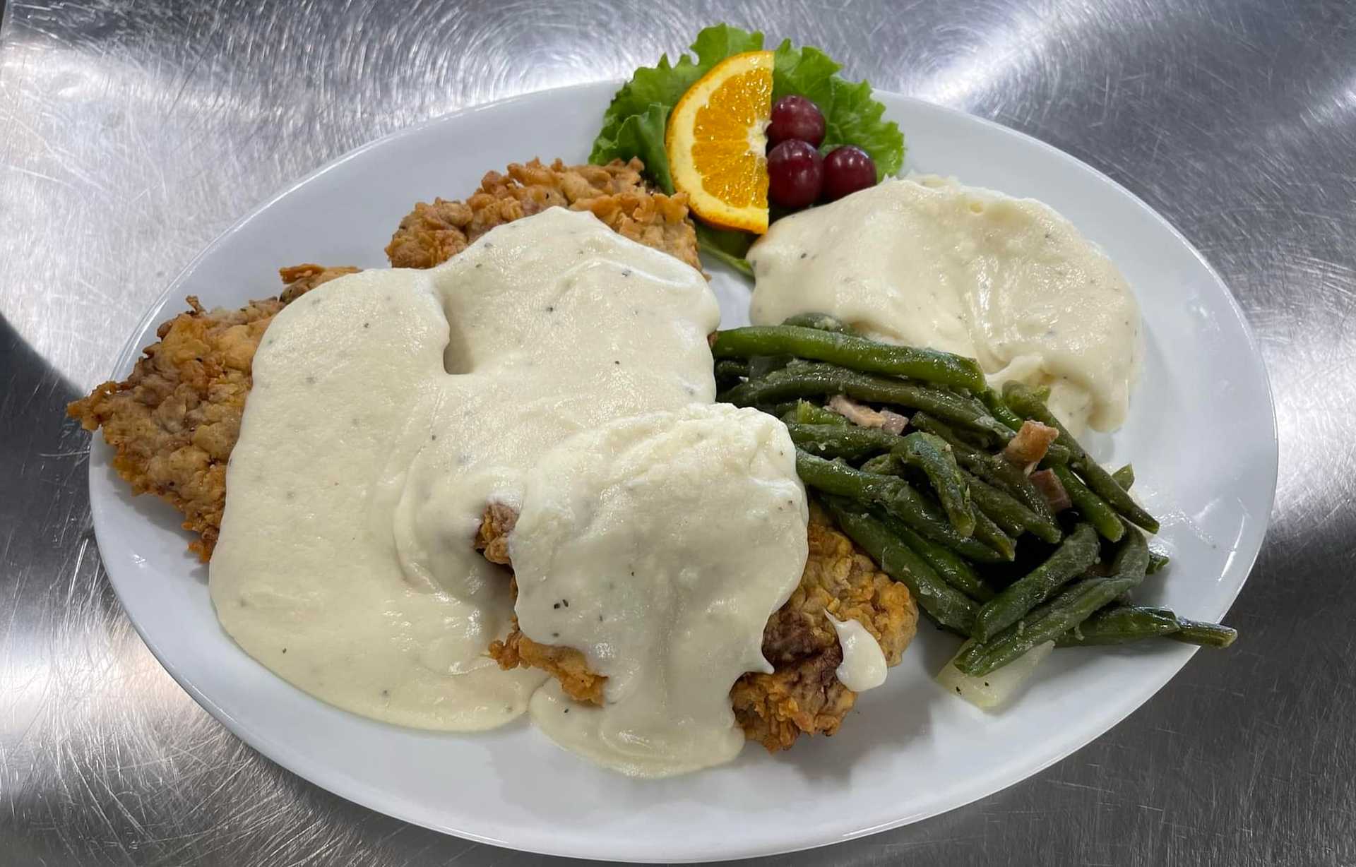 Plate with chicken fried steaks, mashed potatoes, green beans, and garnished with orange and grapes.