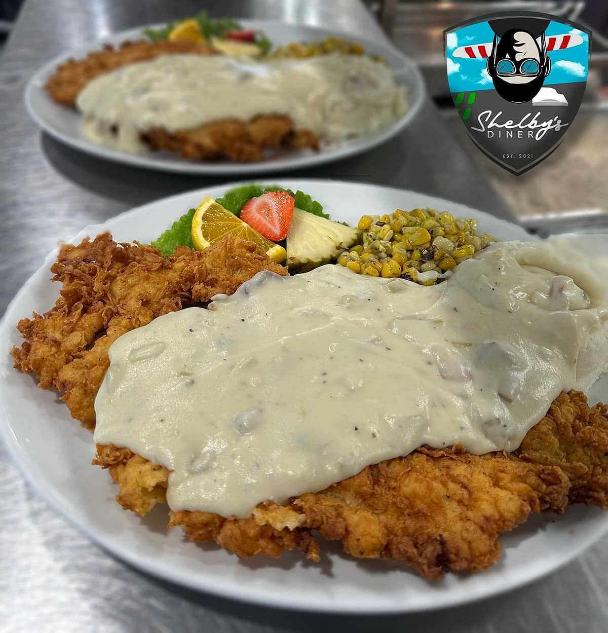 Plates of chicken-fried steak with gravy, mashed potatoes, corn, and fruit garnish at Shelby's Diner.
